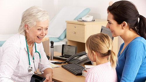 A mother holding a child whilst speaking to a GP